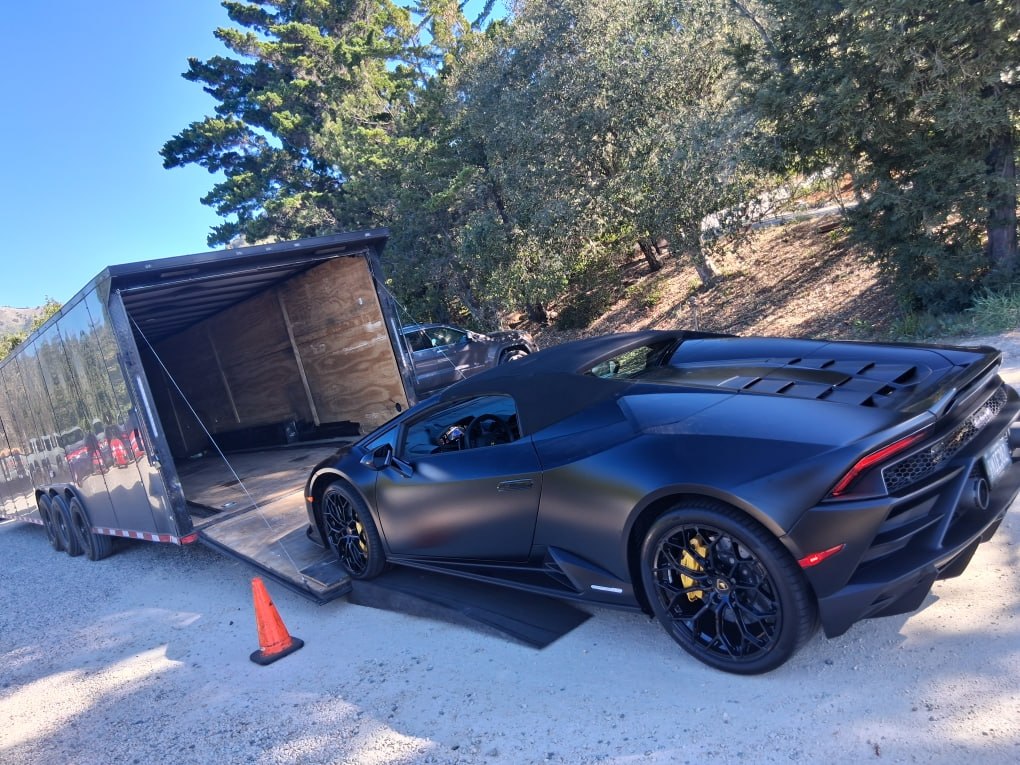 A matte black Lamborghini Huracán being winched onto an enclosed car hauler.