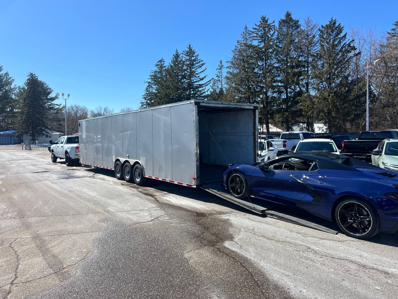 A blue Chevrolet Corvette mid-load on the ramp of an enclosed car hauler.